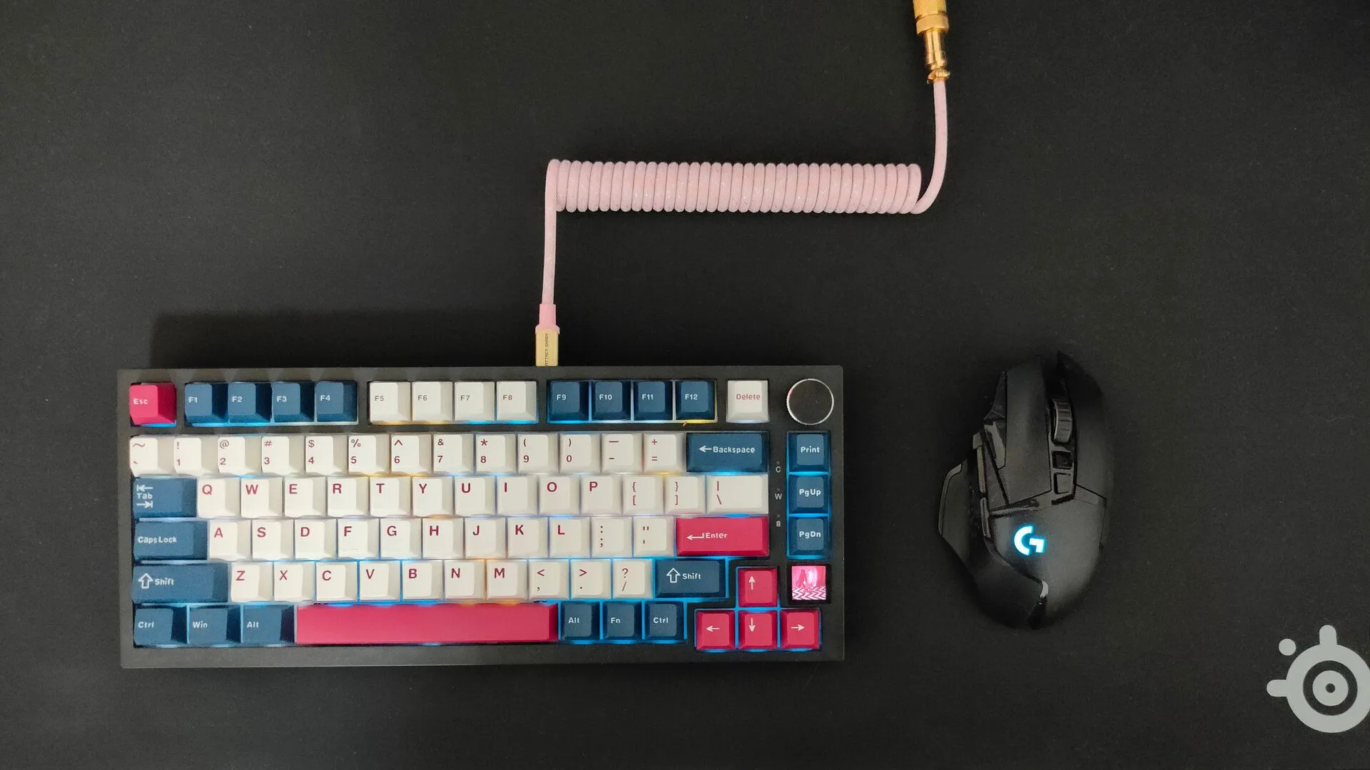 Bàn phím cơ có dây cáp xoắn màu hồng và chuột không dây Logitech G502 trên bàn di chuột SteelSeries QcK, minh họa sự kết hợp có dây/không dây.