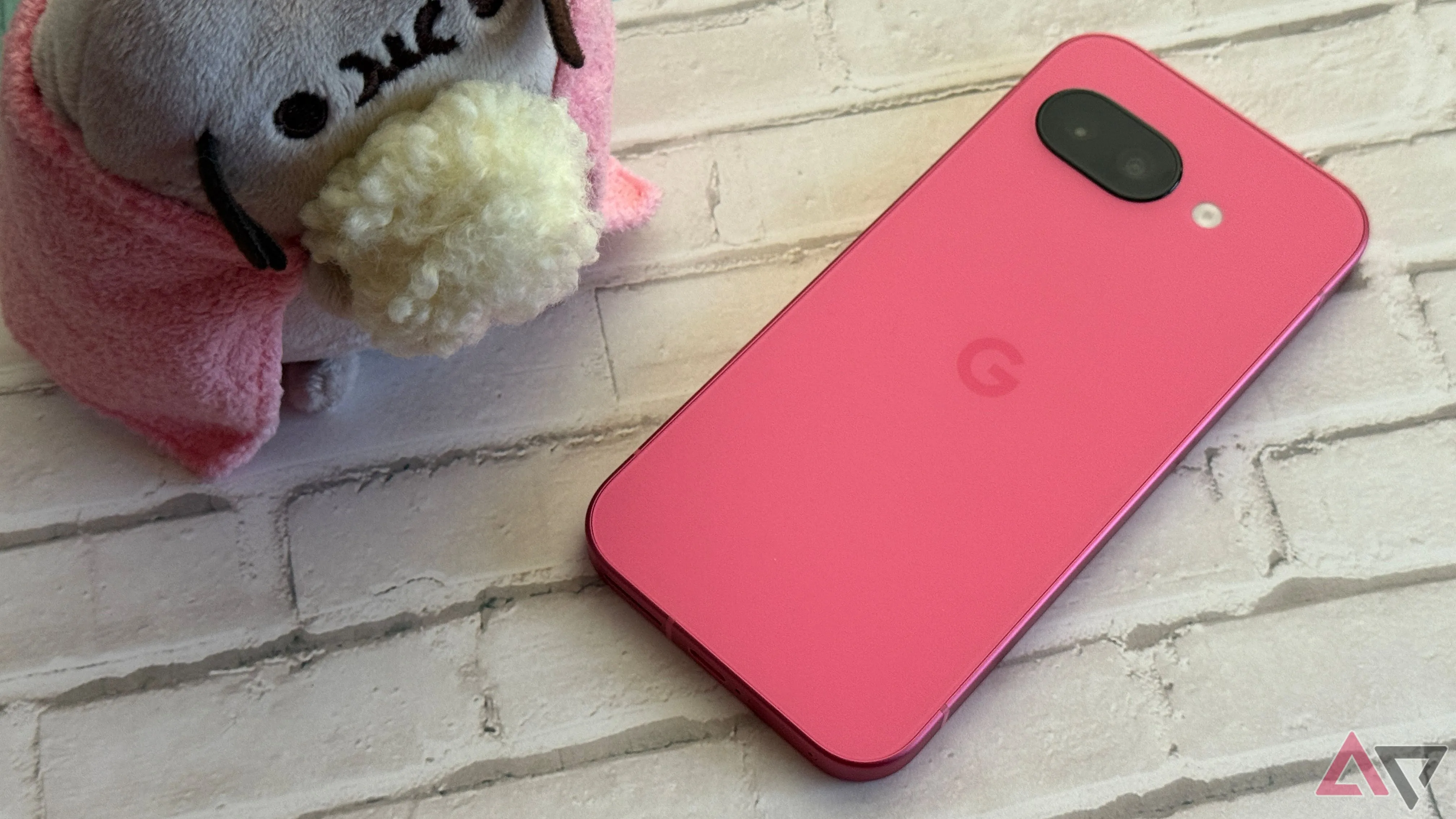 Điện thoại Google Pixel 9a màu hồng Peony cùng đồ vật trang trí trên bàn.