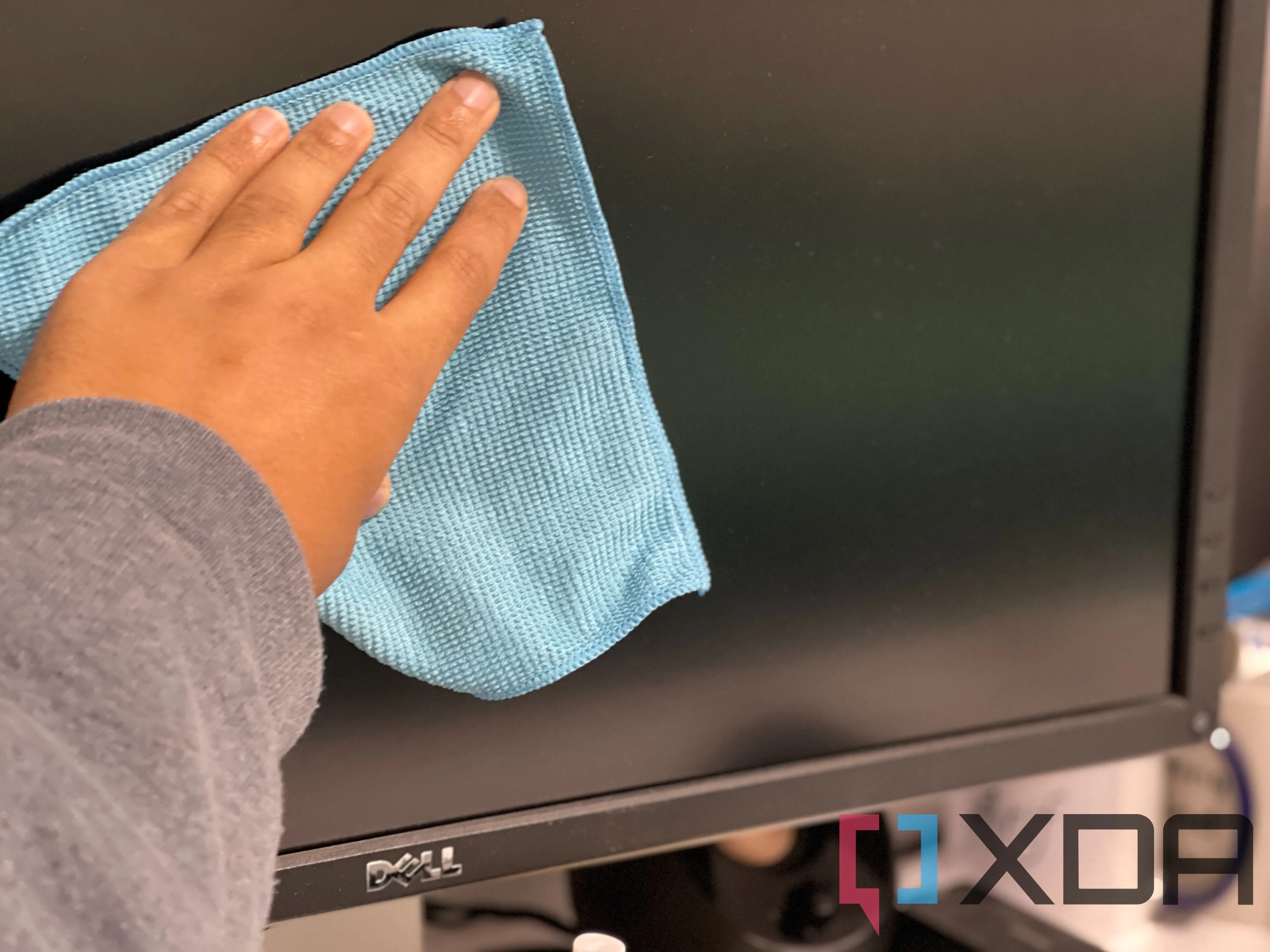 Một người đang cẩn thận lau màn hình OLED máy tính bằng khăn mềm chuyên dụng.