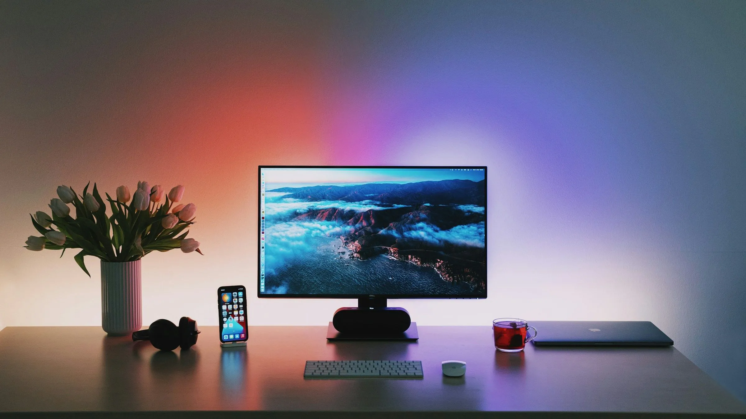 Bàn làm việc với bộ PC được quản lý cáp gọn gàng, có ánh sáng đèn nền phía sau màn hình, tạo không gian làm việc và giải trí thẩm mỹ, sạch sẽ.