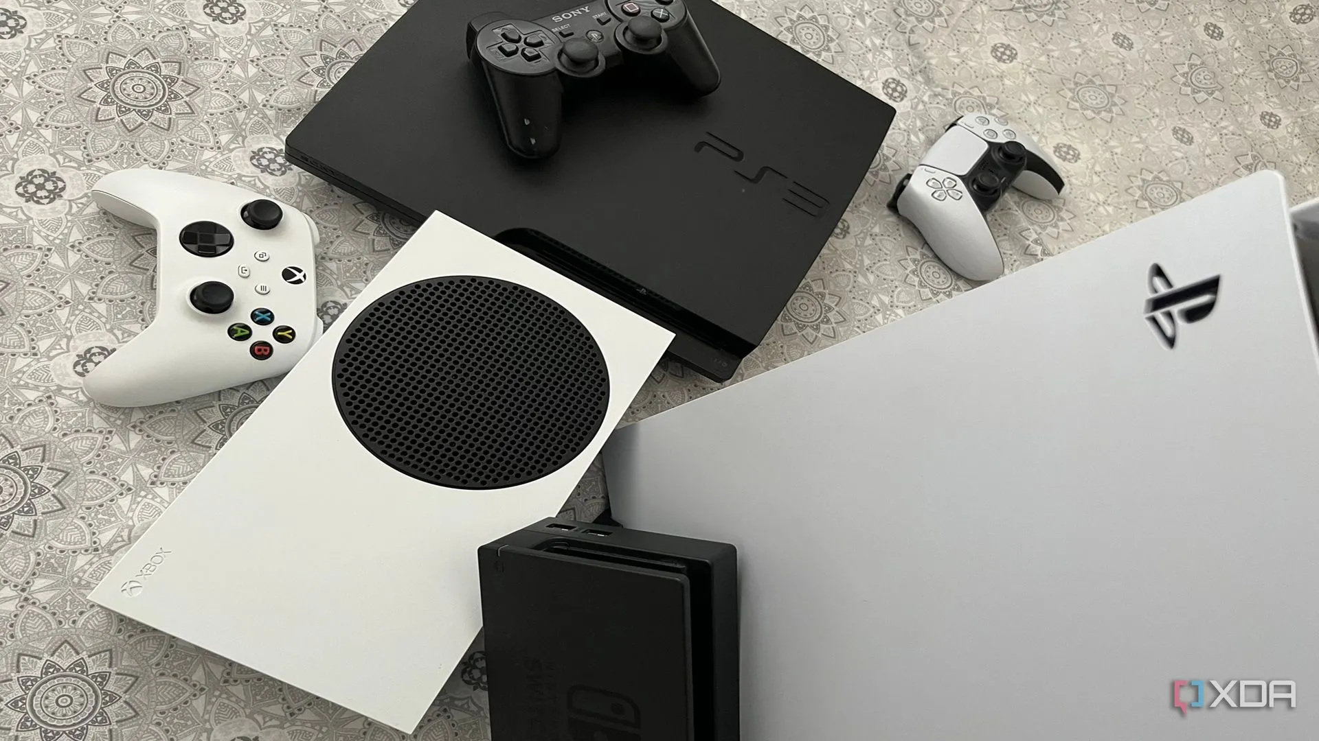 Bộ sưu tập các máy chơi game bao gồm PlayStation 5, Xbox Series X, dock Nintendo Switch và PlayStation 3, tượng trưng cho sự đa dạng của ngành công nghiệp console.
