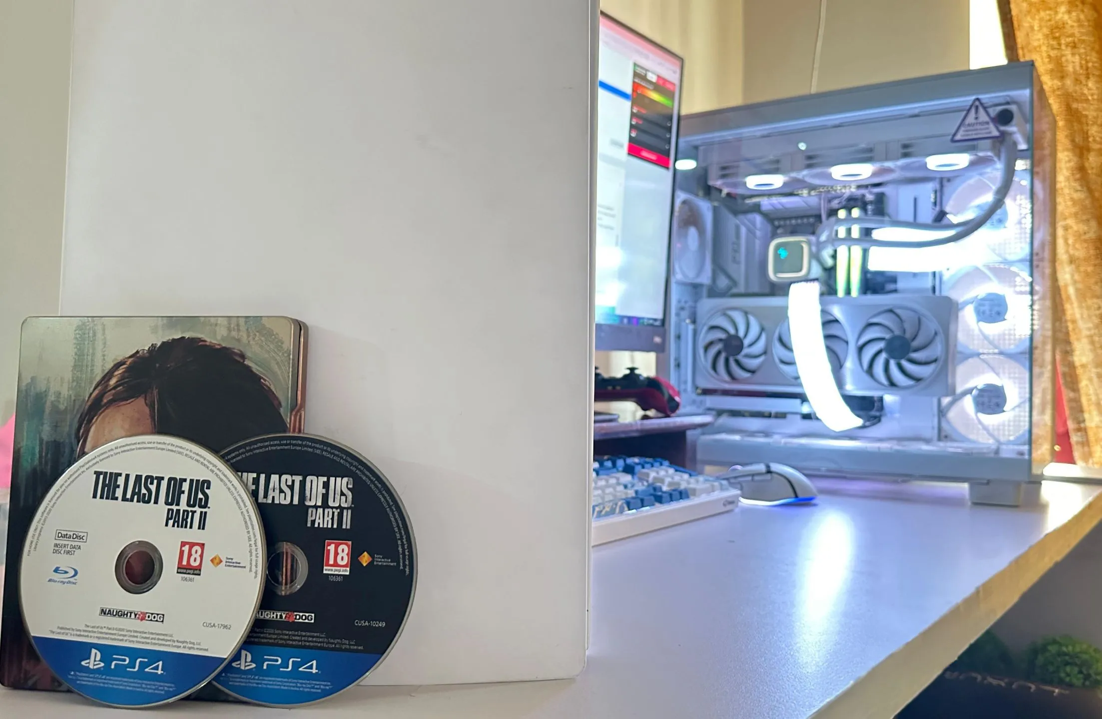Hai đĩa game The Last of Us Part II phiên bản PS4 đặt cạnh một PC và PS5, minh họa dung lượng game lớn cần nhiều đĩa.