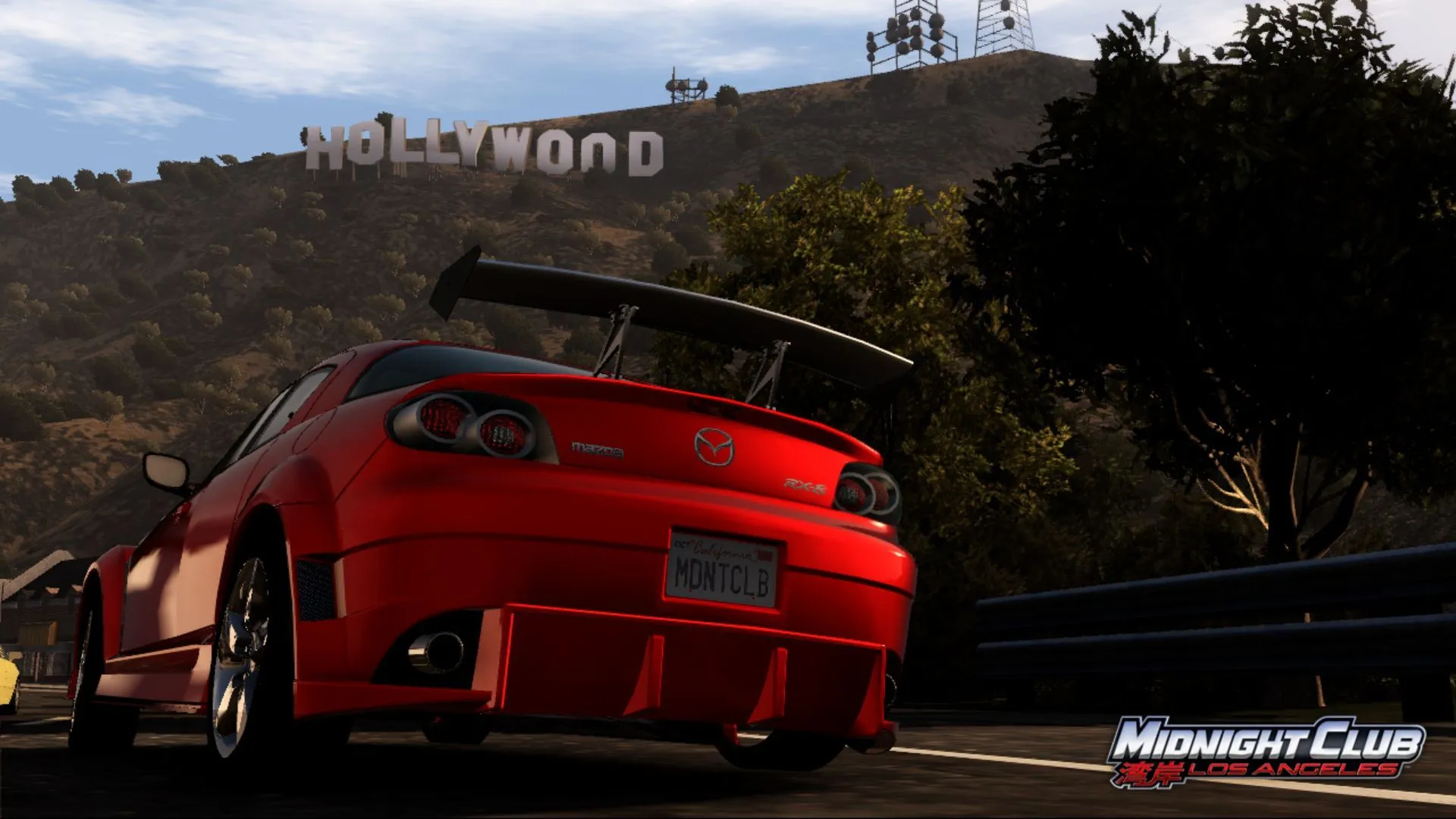 Khoảnh khắc từ Midnight Club: Los Angeles với xe Mazda màu cam đang đua trên đường phố, phía xa là biểu tượng Hollywood, minh họa phong cách đua xe của dòng game Midnight Club