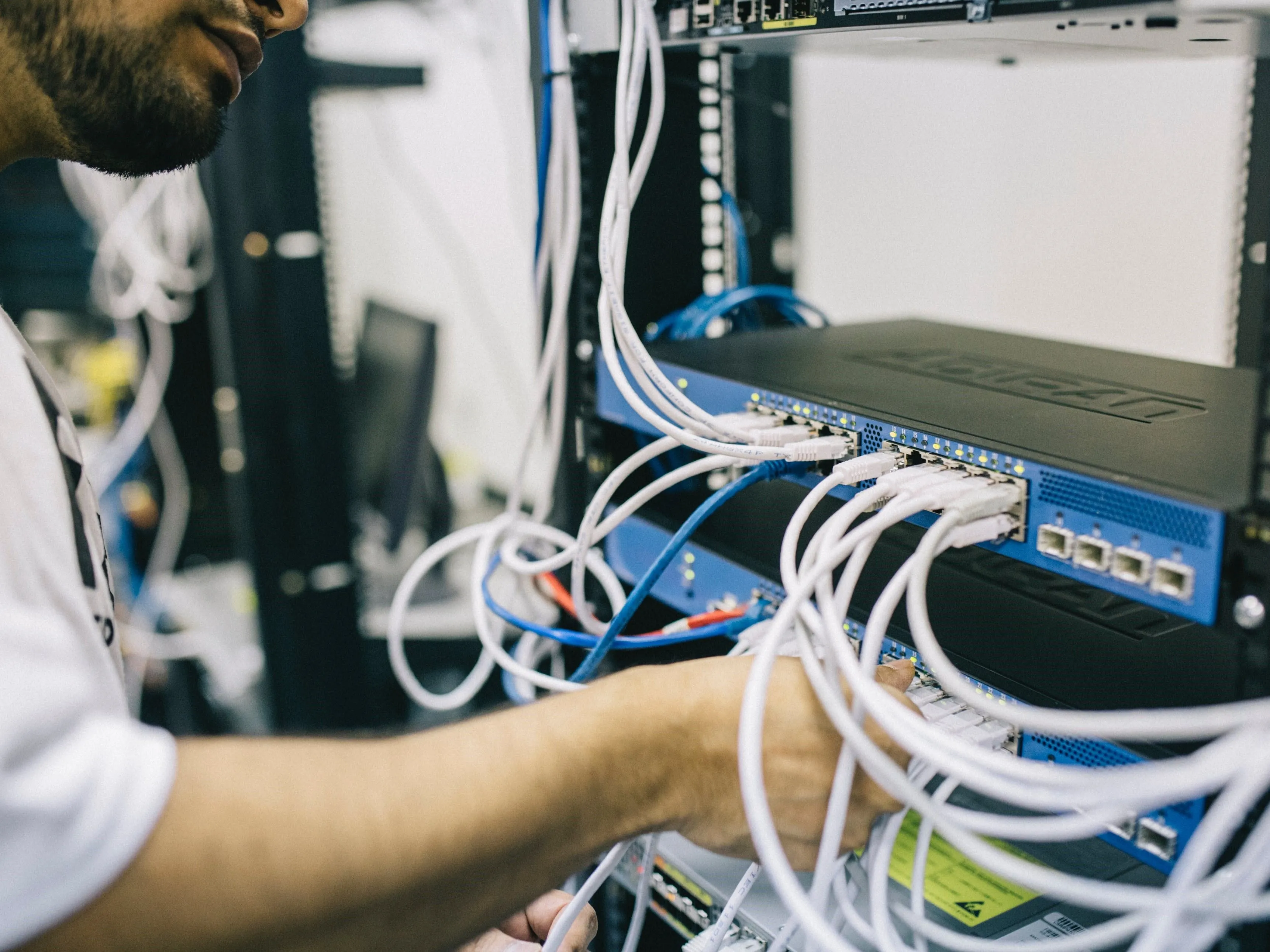 Kỹ sư đang cắm cáp Ethernet vào thiết bị mạng, tượng trưng cho việc quản lý và cập nhật hệ thống mạng.
