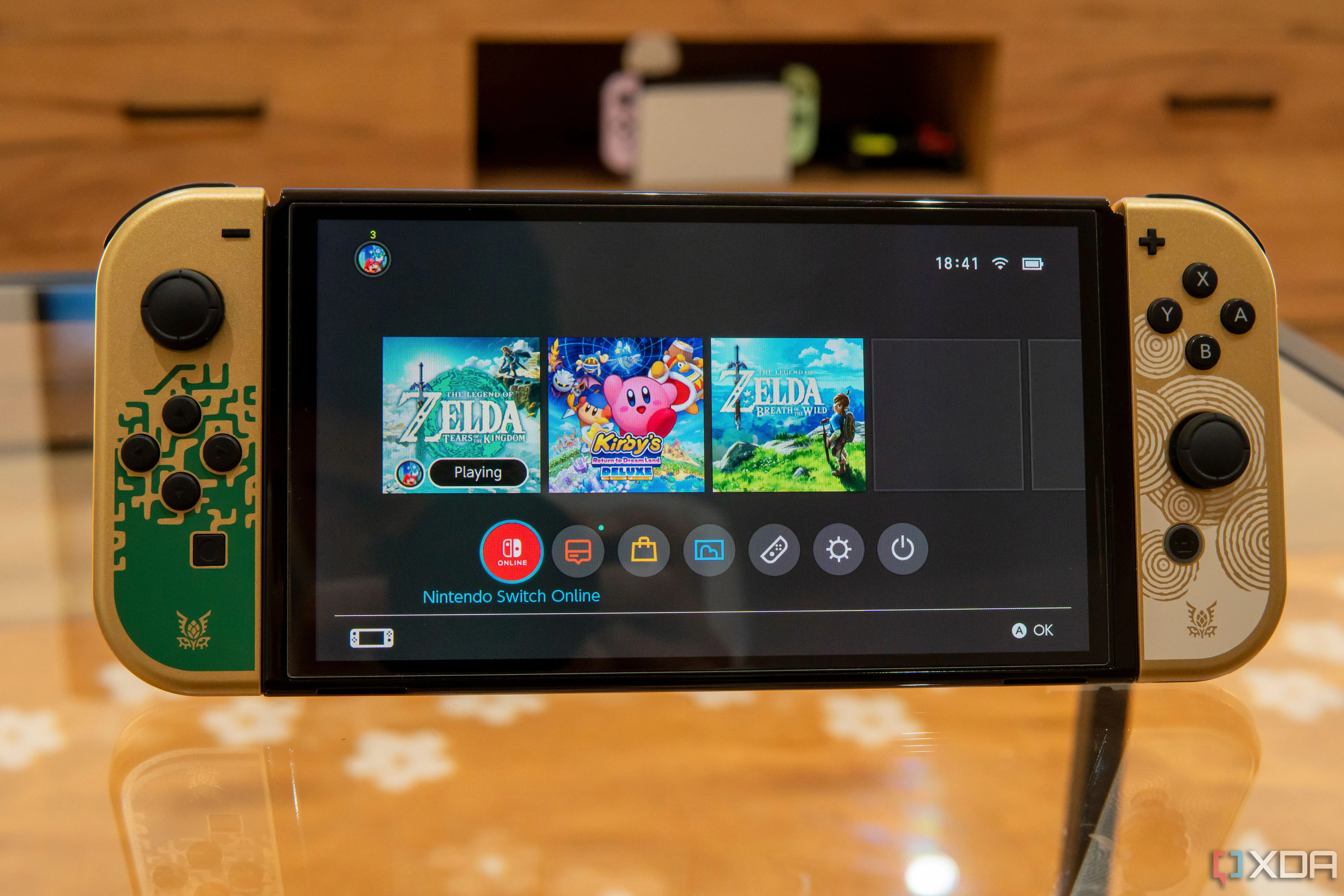 Mặt trước của Nintendo Switch OLED hiển thị menu Home với một trò chơi đang chạy ở nền