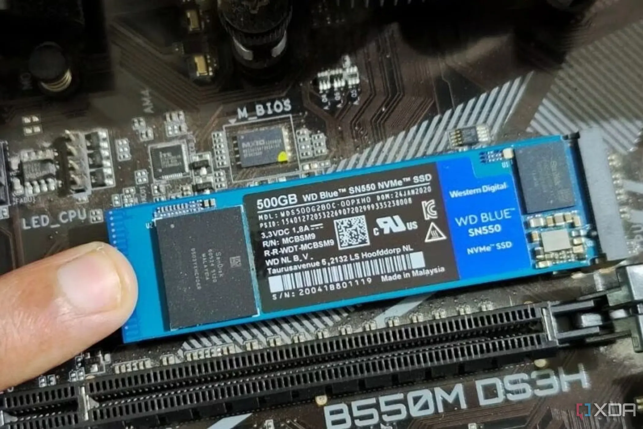 Một người đang giữ cố định ổ cứng SSD M.2 trên bo mạch chủ bằng ngón tay trước khi cố định bằng ốc vít.