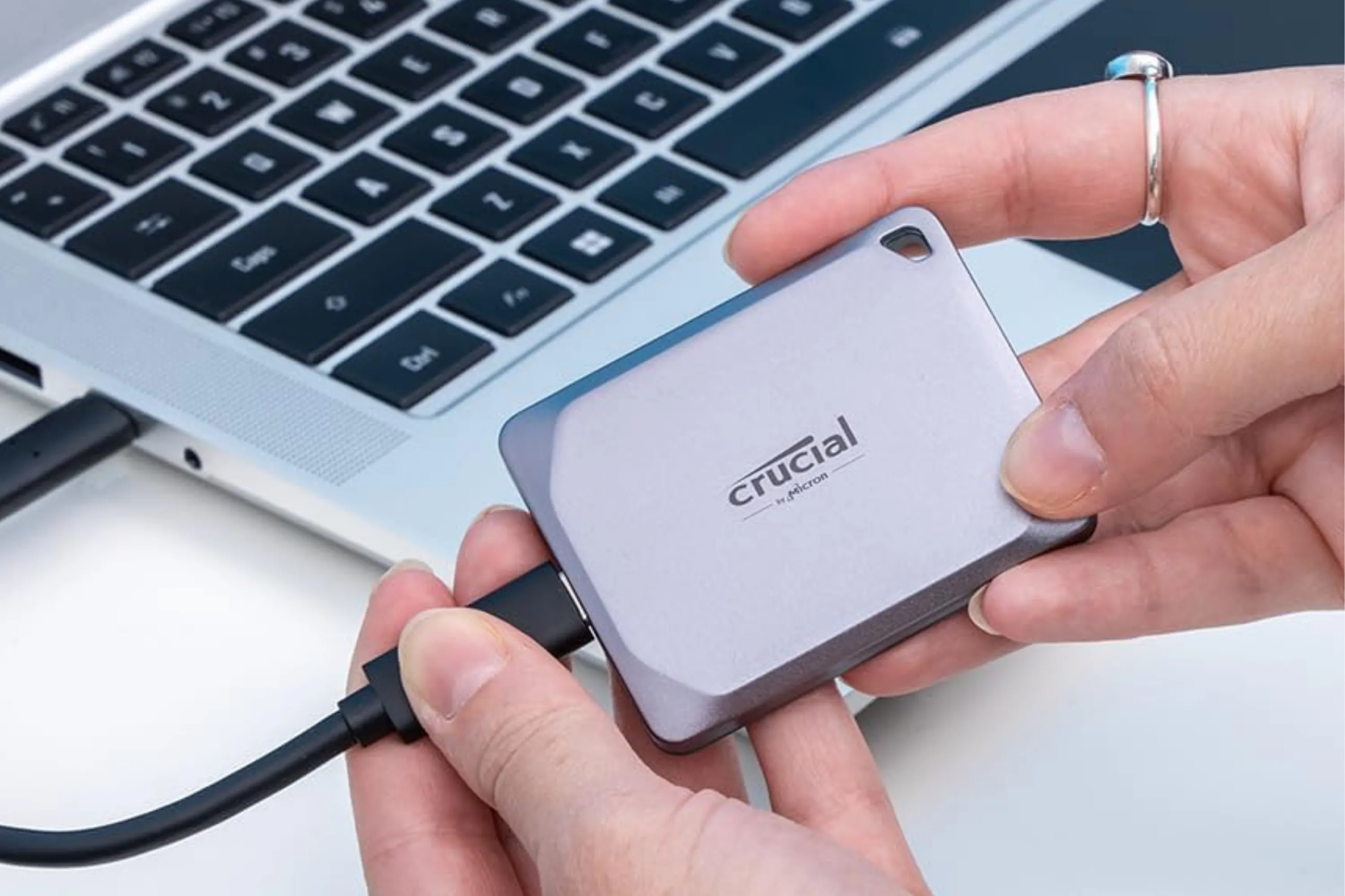 Ổ SSD di động Crucial X9 Pro 4TB nằm gọn trong lòng bàn tay bên cạnh laptop