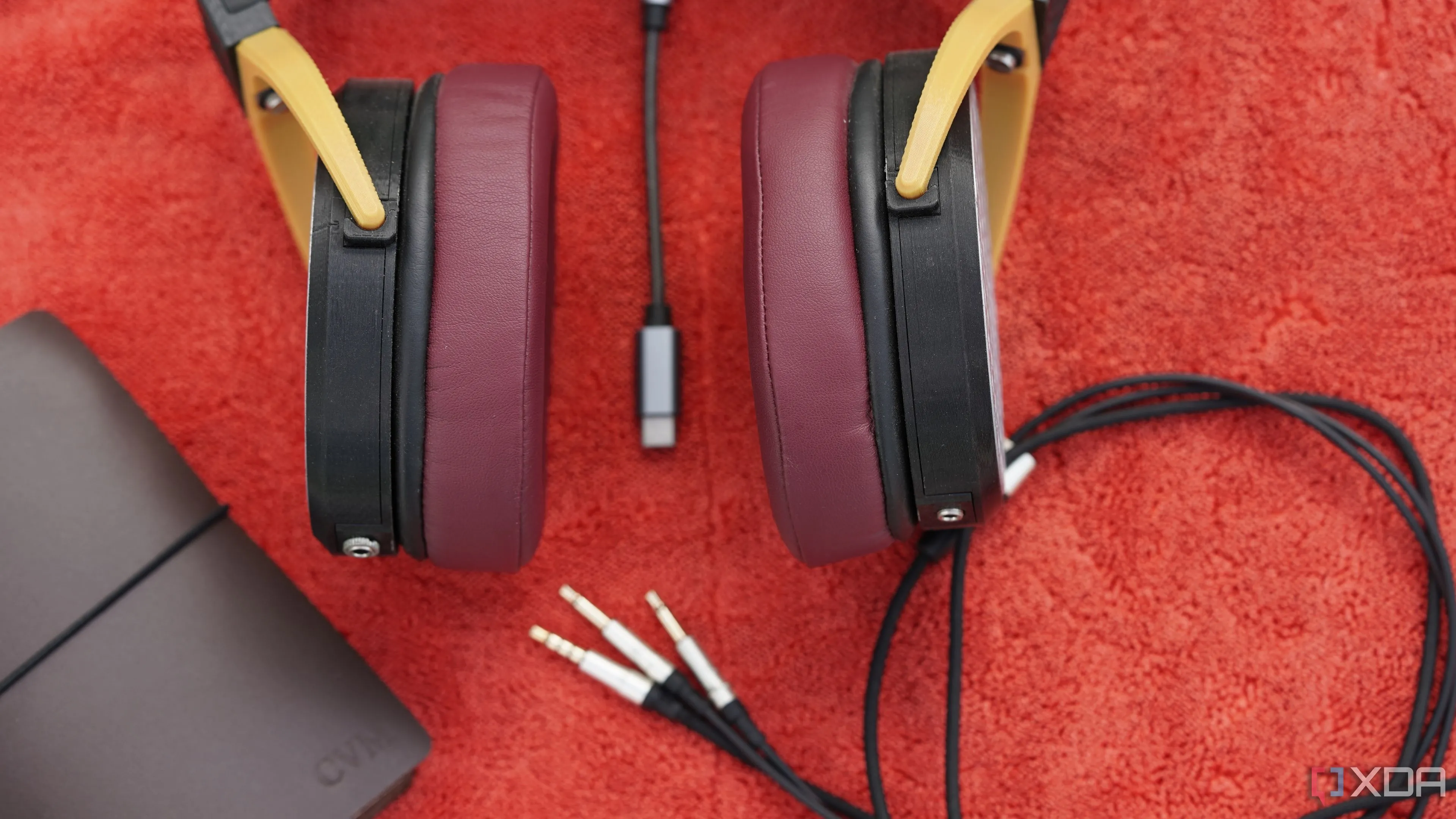 Tai nghe 3D in dạng open-back cùng cáp audio đặt cạnh sổ tay trên thảm đỏ, minh họa các biến số âm thanh