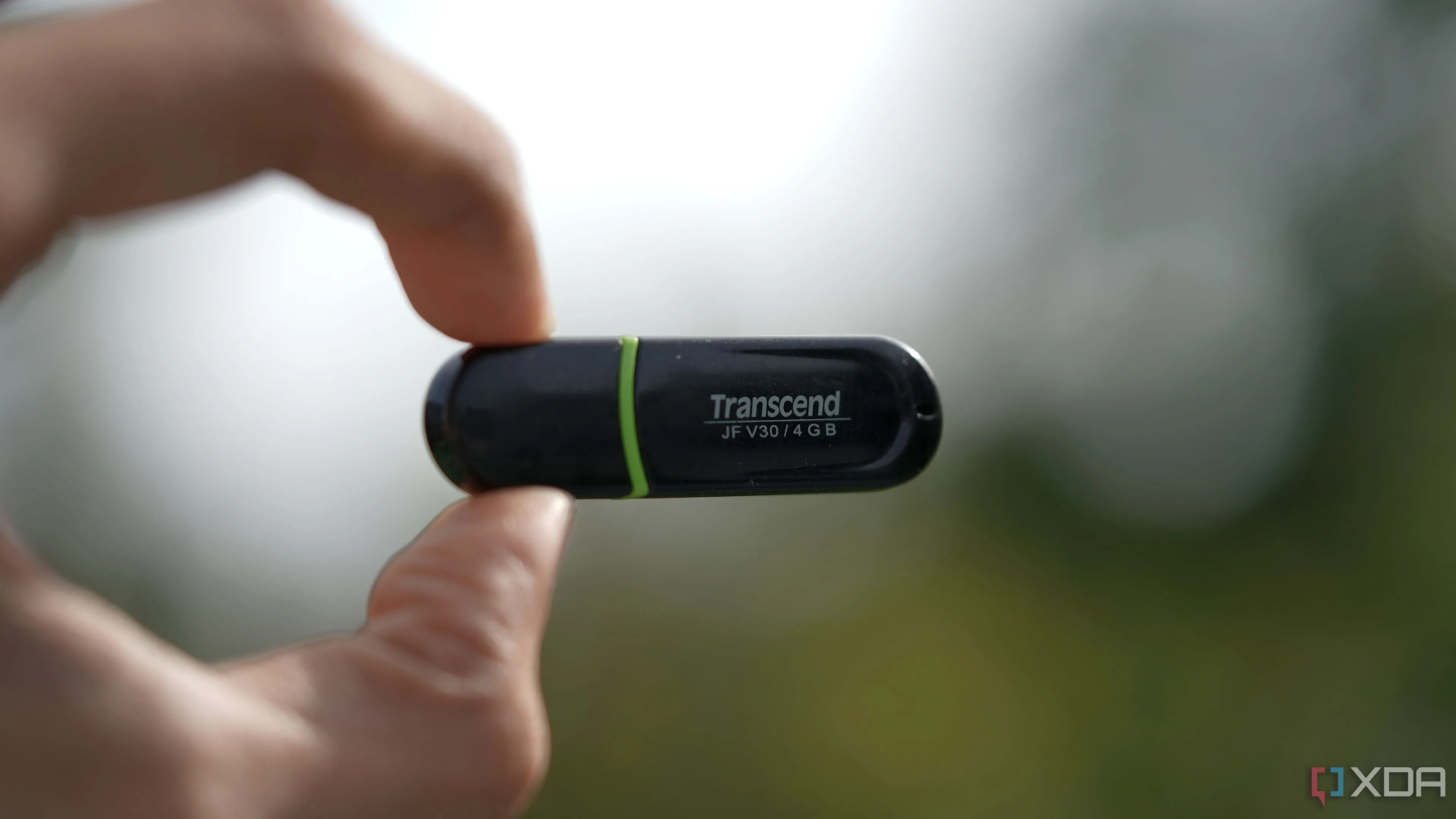 USB drive Transcend 4GB được kẹp giữa các ngón tay, với nền mờ